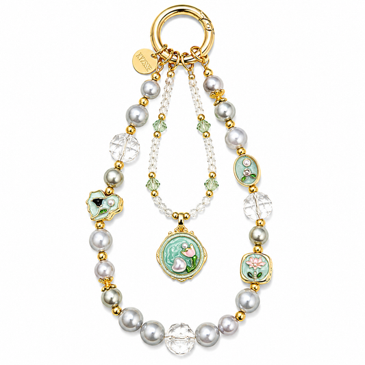 A gold-tone key ring bag charm featuring faux pearls, clear crystal beads, and multiple green enamel medallions with floral and bird motifs, shown on a plain white background.