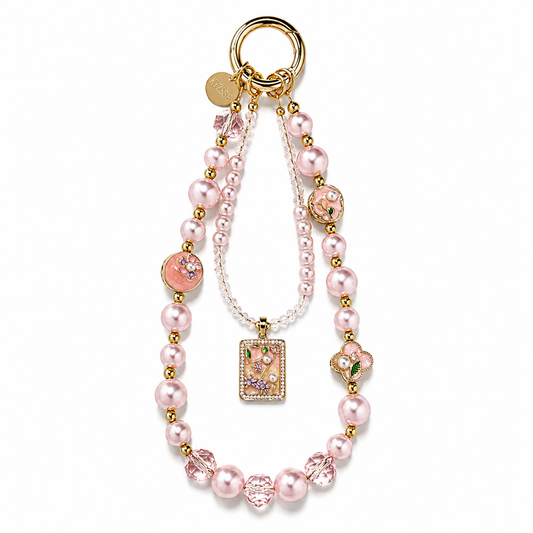 A pink and gold beaded charm strap with pearl-like beads, clear rhinestone accents, a floral pendant, and a gold key ring on a white background.